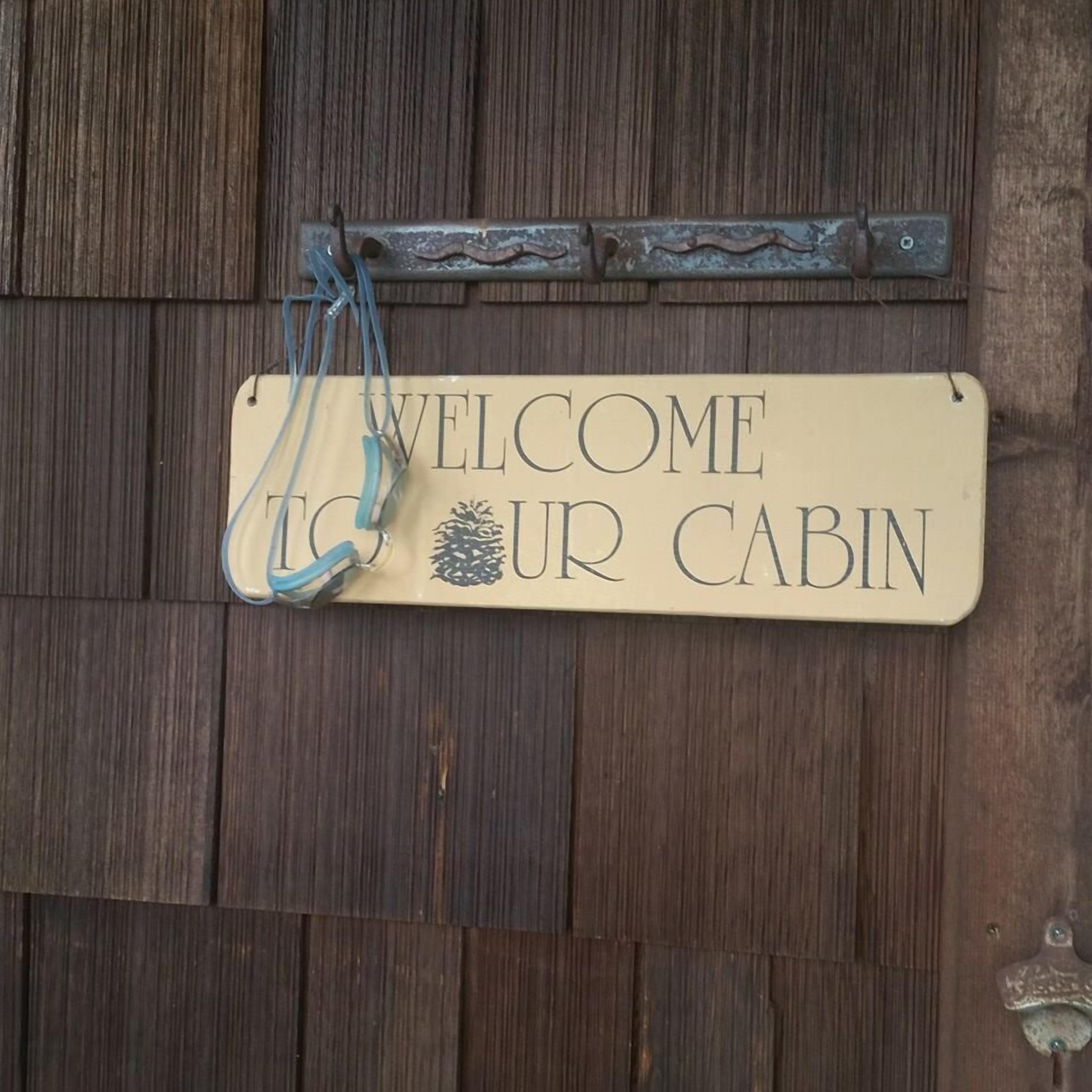 Uma porta de madeira com uma placa que diz 'WELCOME TO OUR CABIN'.