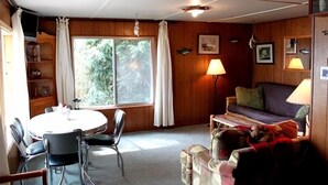 Een knus ingerichte kamer met een ronde tafel, stoelen, een bank en twee lampen.