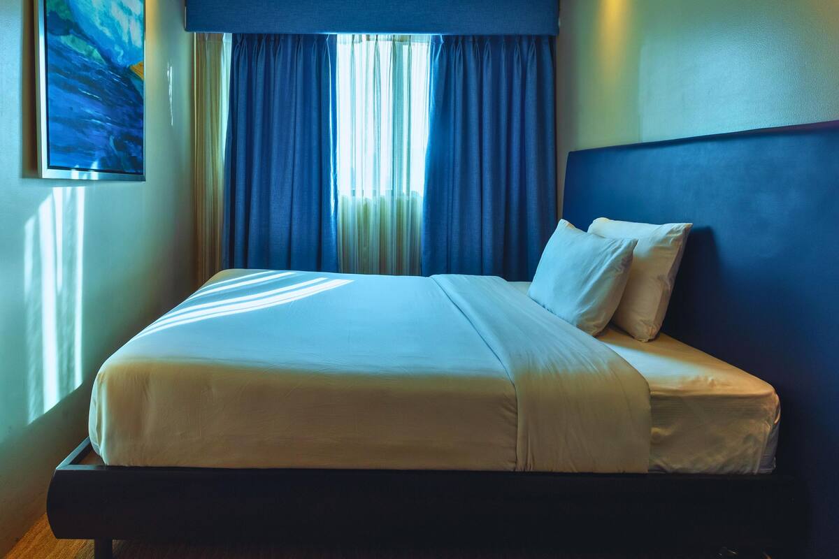 A hotel room with a bed, curtains, and a painting on the wall.