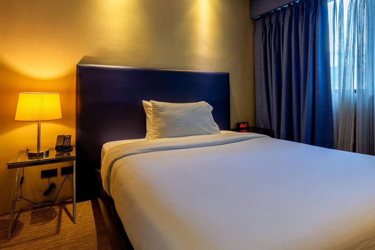 A hotel room with a bed, a bedside table with a lamp, and a nightstand with a phone.