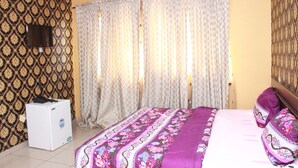 Une chambre à coucher avec un lit, des rideaux, un téléviseur et un appareil électroménager blanc.