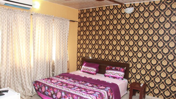 Une chambre à coucher avec un lit, des rideaux, un mur à motifs et un ventilateur de plafond.