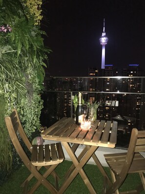 A rooftop terrace with wooden furniture, a bottle of champagne, and a view of the CN Tower at night. - Magical View Homestay at The Robertson (Kuala Lumpur)