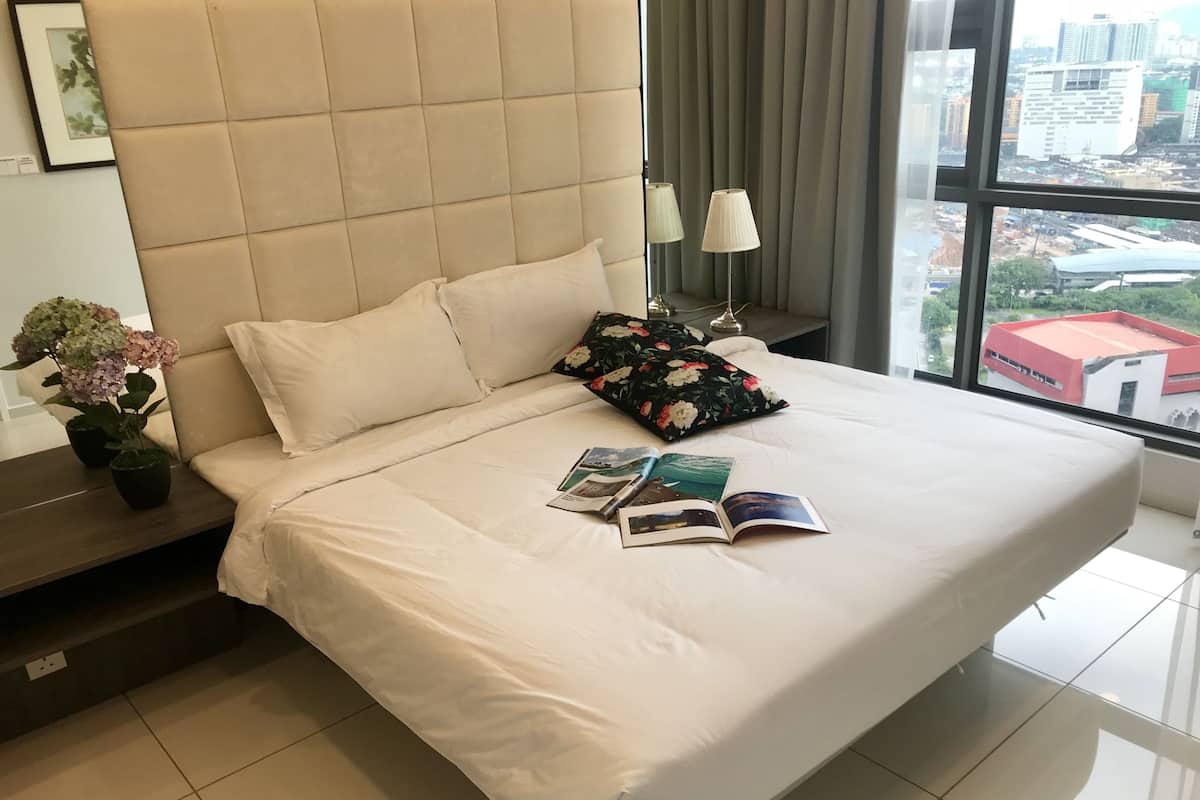 A hotel room with a large bed, a nightstand with a potted plant, a window with a city view, and a framed picture on the wall.