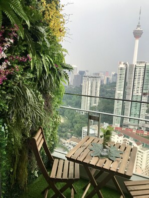 A balcony with a wooden table and chairs, surrounded by lush greenery and a cityscape view. - Magical View Homestay at The Robertson (Kuala Lumpur)