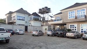A parking lot with several cars and a building with a water tank on the roof. - Alheri Suites (Ibadan)