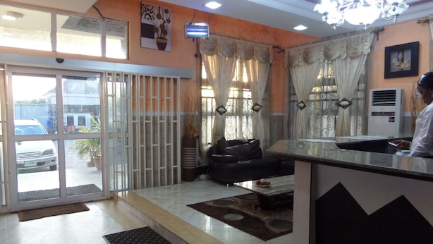 A reception area with a glass door entrance, a sofa, a small rug, and a desk. - Alheri Suites (Ibadan)