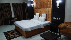 A bedroom with a bed, a nightstand, a chair, and a desk. - Alheri Suites (Ibadan)
