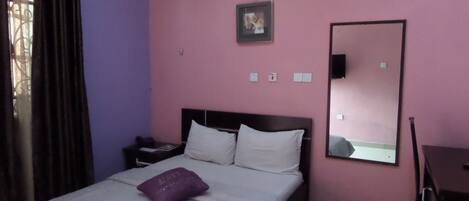 A hotel room with a bed, a nightstand, a dresser, a mirror, and an air conditioning unit on the wall.