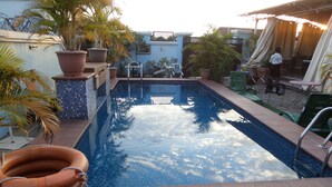 A swimming pool with a tiled edge, surrounded by potted plants and outdoor furniture. - Alheri Suites (Ibadan)