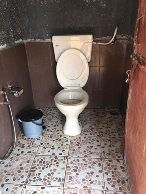A small, tiled bathroom with a toilet, a bucket, and a shower. - Stay In Pawana Camp (Mawal)