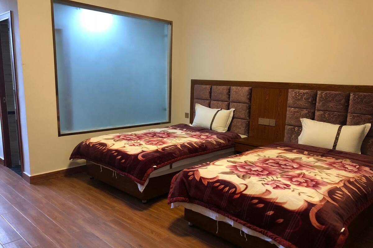 Une chambre d’hôtel avec deux lits, chacun recouvert d’une couvre-lit à motifs floraux, une grande fenêtre et un plancher en bois.