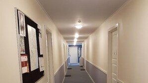 A hallway with a bulletin board on the left, doors on both sides, and a white table at the end.