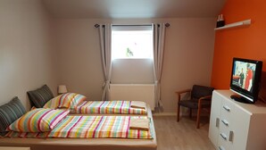 A bedroom with two beds, a desk, a chair, a TV, and a window with curtains.