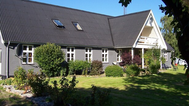 A large, two-story building with a dark roof, multiple windows, and a well-maintained garden with various plants and a lawn.