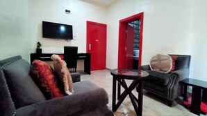 A living room with a sofa, armchair, and a small table. There is a TV mounted on the wall, a red door, and a black chair. - BoardWalk Hotel Wuse 2 (Abuja)