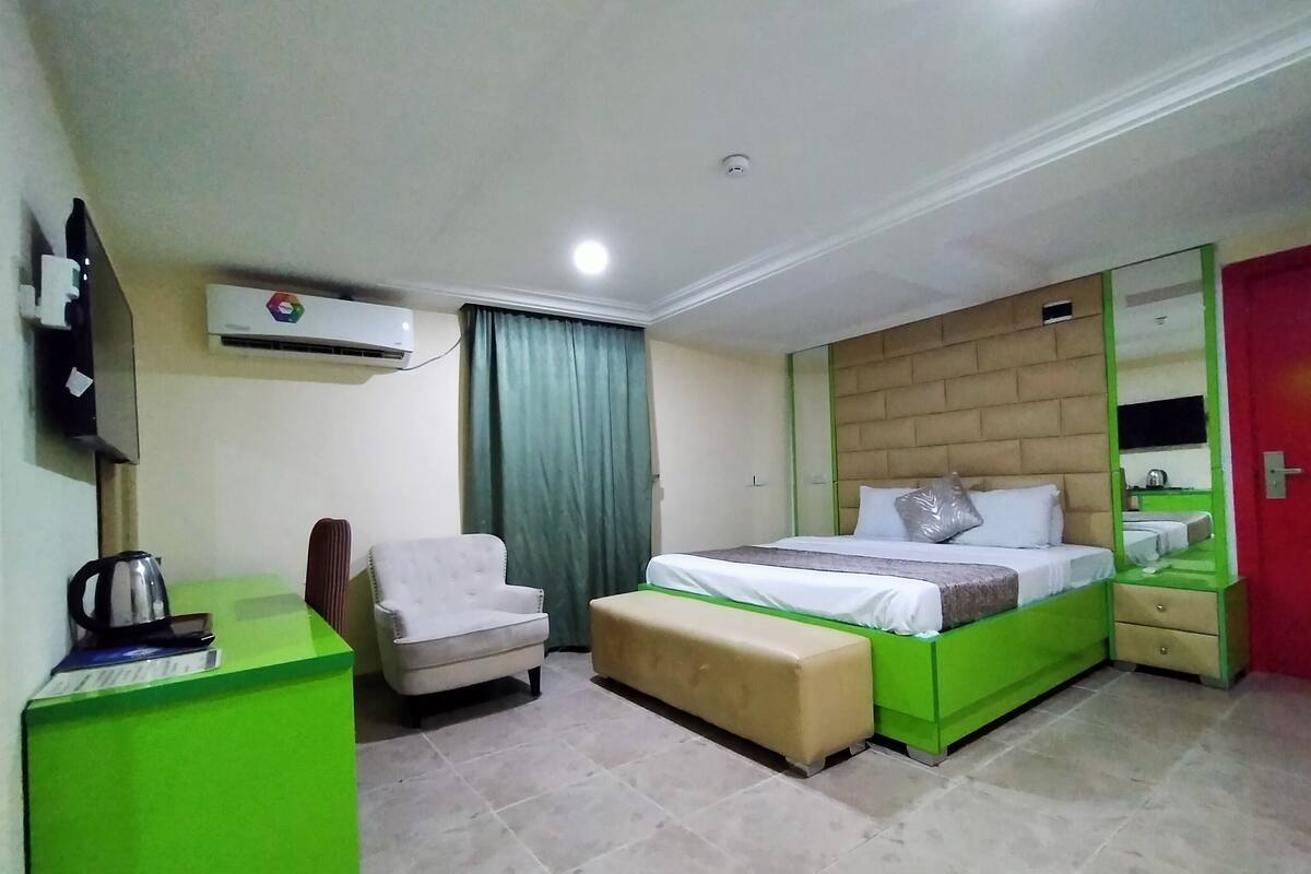 A hotel room with a bed, a chair, a desk, and a mirror.
