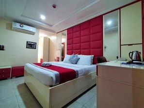 A hotel room with a bed, a bedside table, a mirror, and a red headboard.