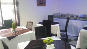 A dining area with round tables covered in white tablecloths, black chairs, and a small potted plant on one table. - BoardWalk Hotel Wuse 2 (Abuja)