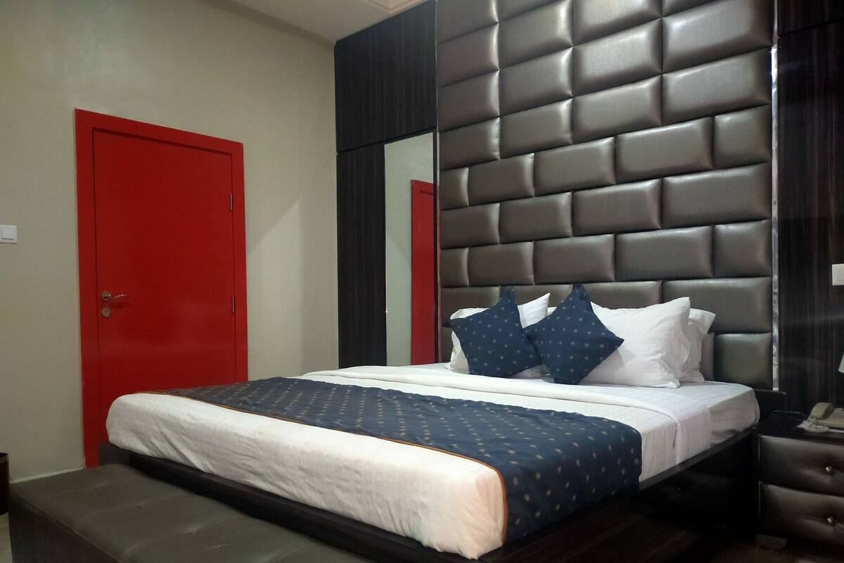 A bed with a headboard, a bench, a red door, and a mirror.