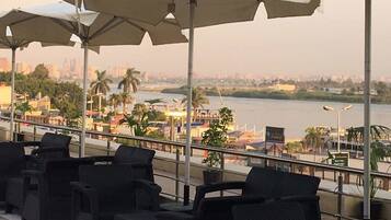 Outdoor seating with umbrellas, overlooking a river and cityscape.