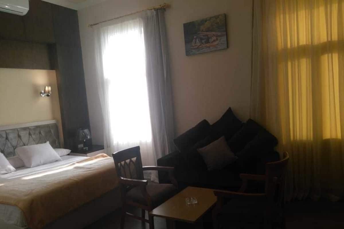 A hotel room with a bed, a sofa, a small table, and a painting on the wall.