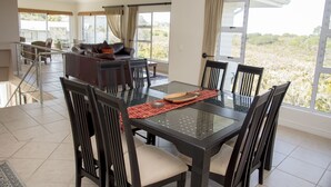 A dining area with a glass table and chairs, a sofa in the background, and large windows with curtains. - 2 Sheerline (Knysna)
