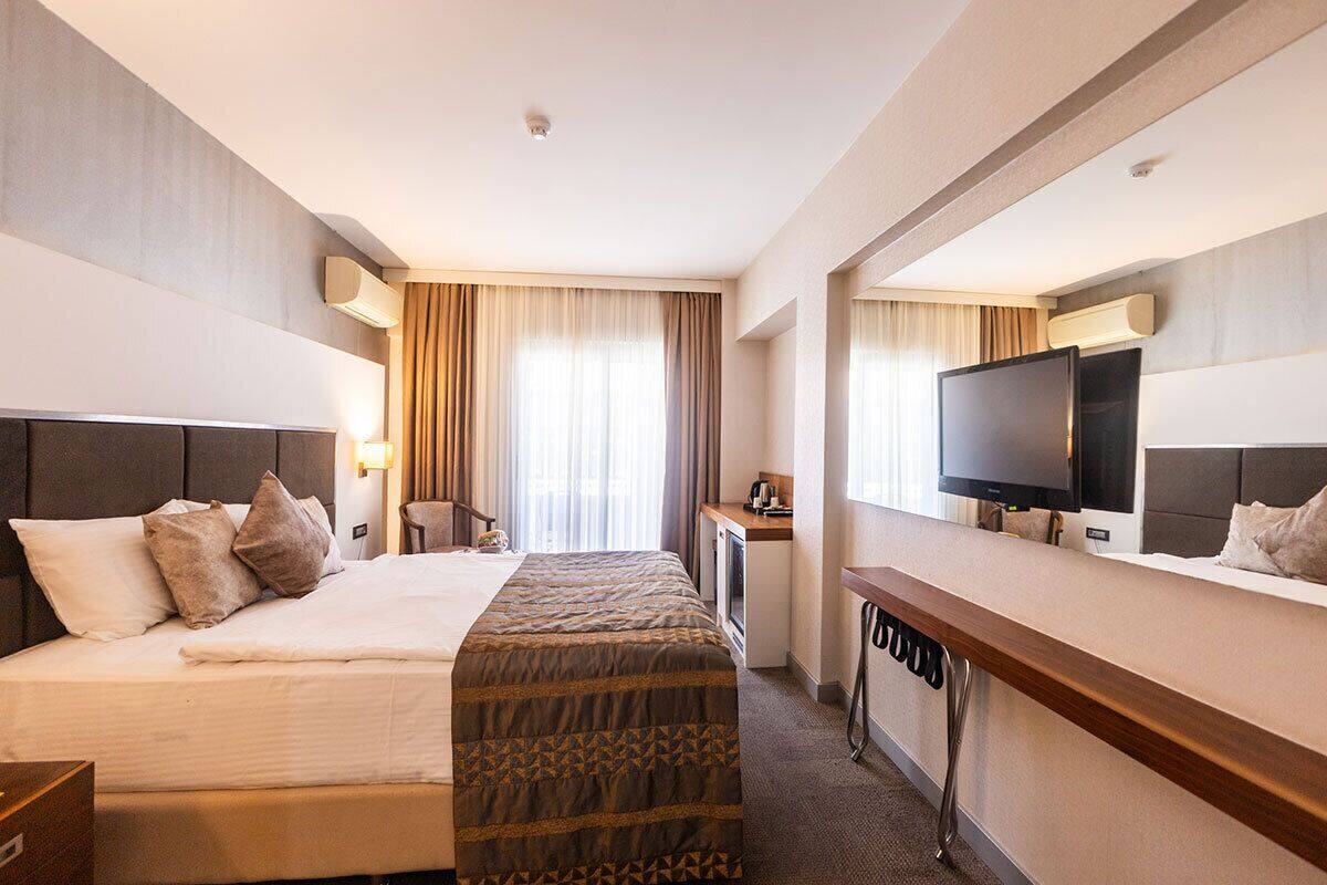 A hotel room with a bed, a desk, a television, and a window with curtains.