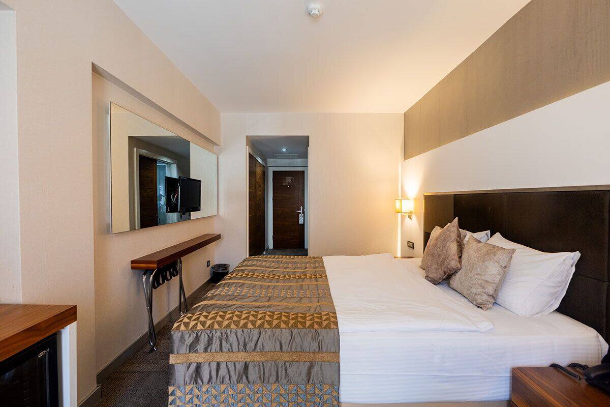 A hotel room with a bed, a desk, a mirror, and a door leading to a hallway.