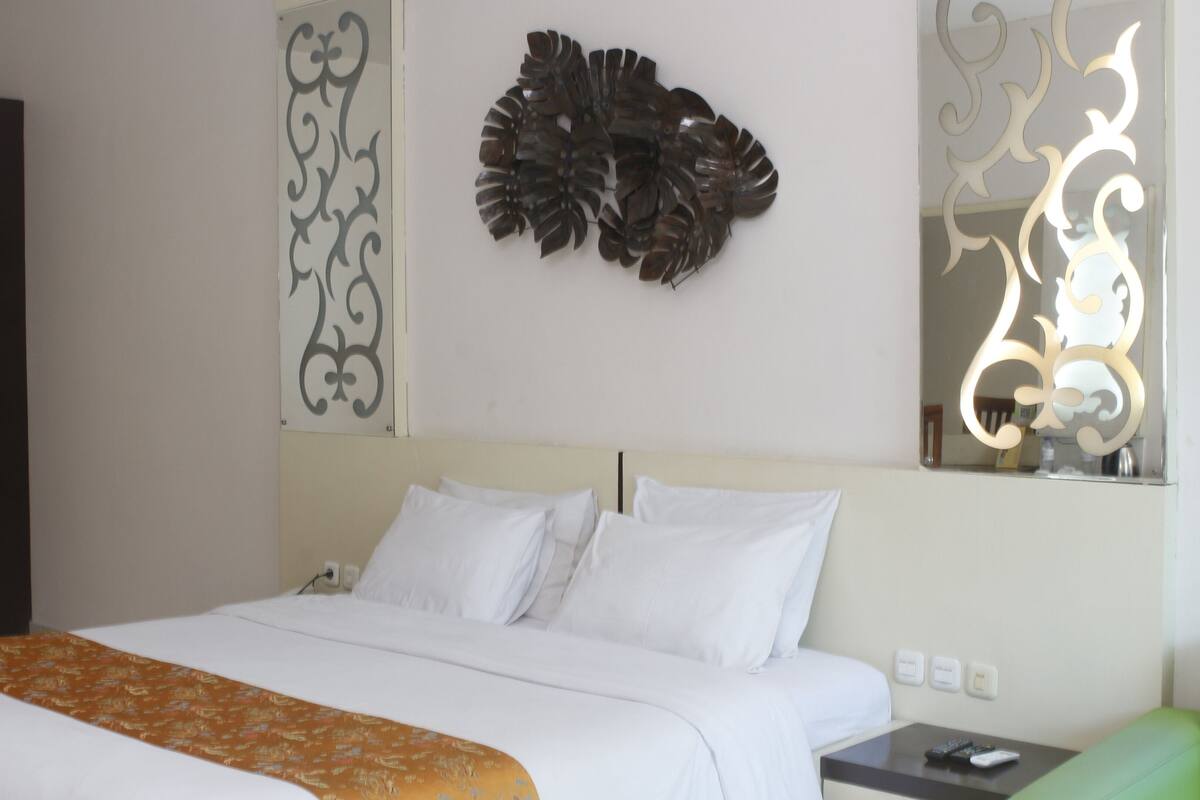 A hotel room with a bed, a nightstand, a green chair, decorative wall art, and a mirror.