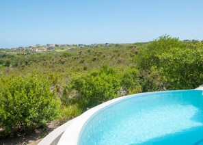 A swimming pool surrounded by lush greenery and a view of a hillside with buildings in the distance.
