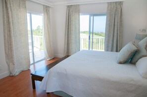 A bedroom with a large bed, a wooden bench, and a balcony with curtains.