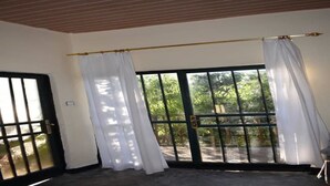 A room with a large sliding glass door leading to a garden, a wooden ceiling, and a white curtain.