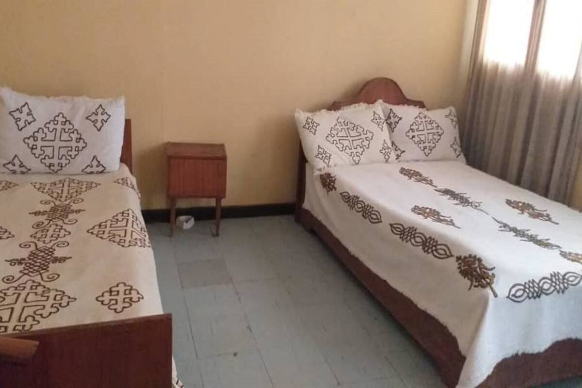 A room with two beds, each with patterned bedding. There is a small wooden nightstand between the beds.