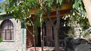A stone building with a wooden door and windows, surrounded by trees and a stone wall.