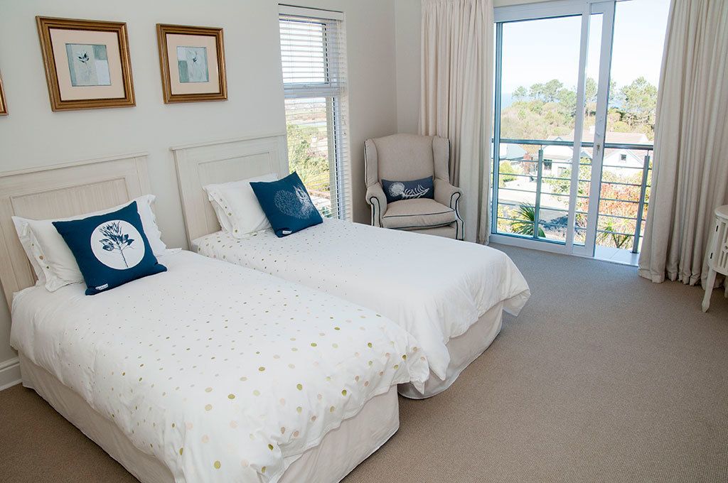 A bedroom with two beds, a chair, and a large window with curtains.