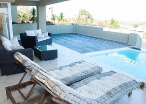 A rooftop pool area with lounge chairs and a sofa, surrounded by a low wall and a view of the city. - 9 Sheerline (Knysna)