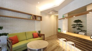 A modern living room with a green sofa, a round table, and a wooden reception desk. - Muguang Inn (Hengchun)