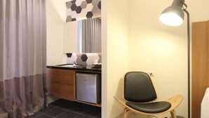 A hotel room with a wooden desk, a chair, a small refrigerator, a mirror with a hexagonal pattern, and a lamp. - Muguang Inn (Hengchun)