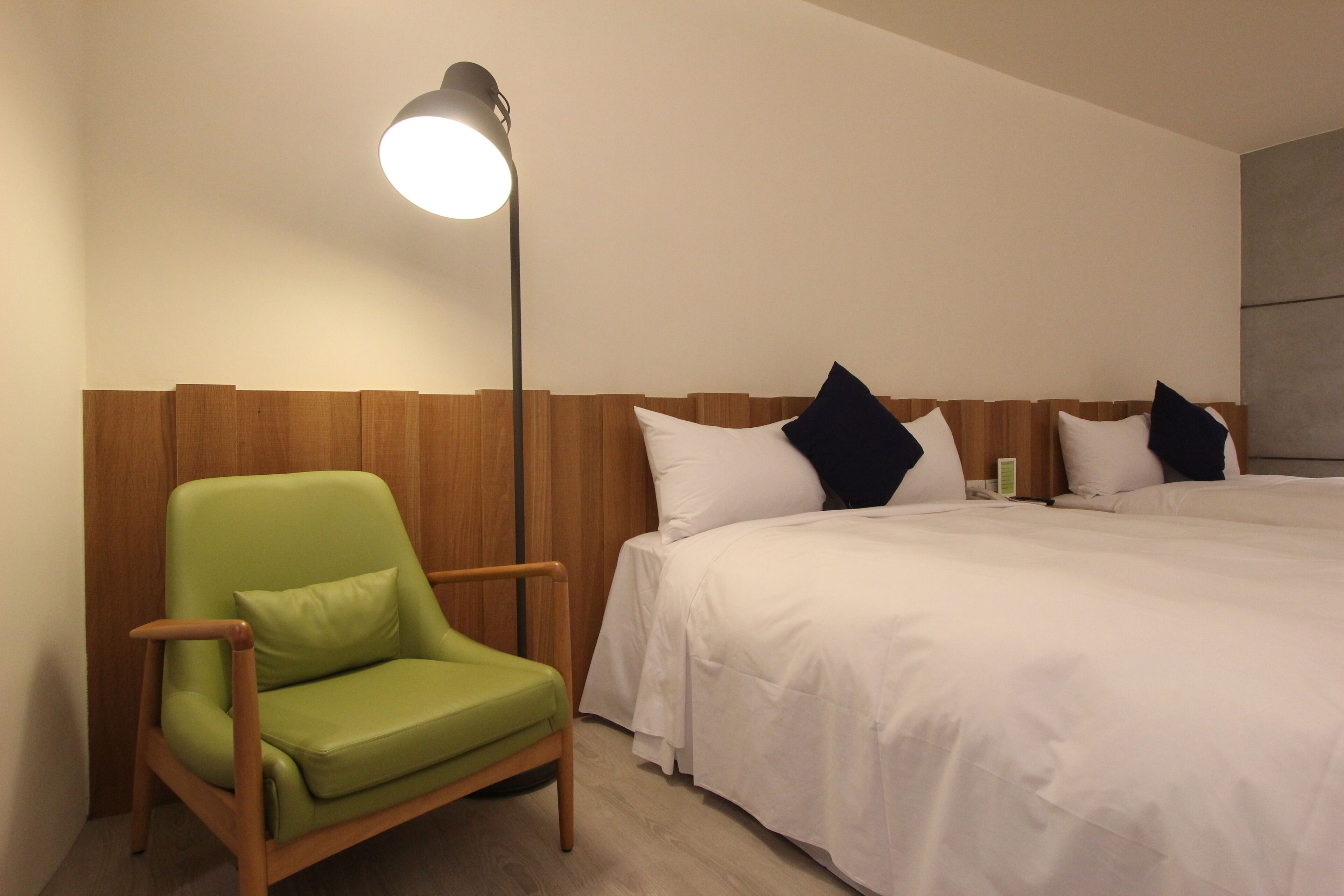 A hotel room with a single bed, a green armchair, and a floor lamp.
