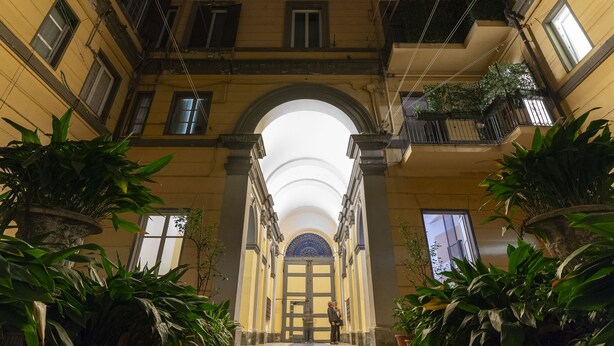 A corridor with a tiled floor leading to a grand archway with a blue patterned door.