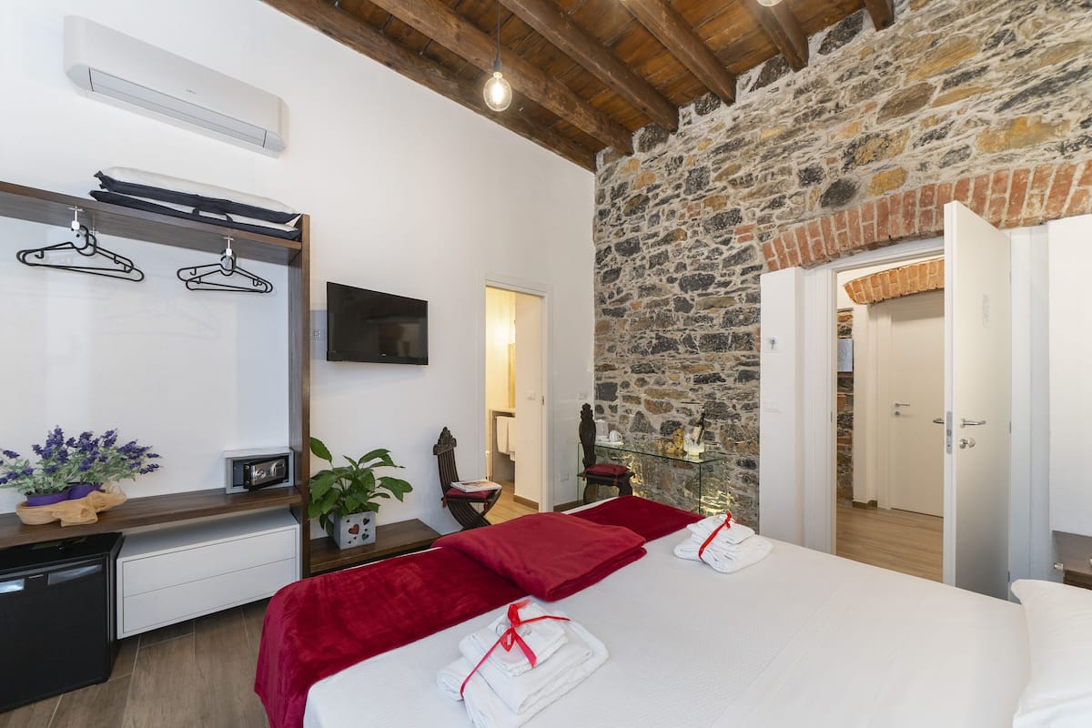 A bedroom with a stone wall, a bed with red bedding, a TV, a mirror, and a wooden ceiling.