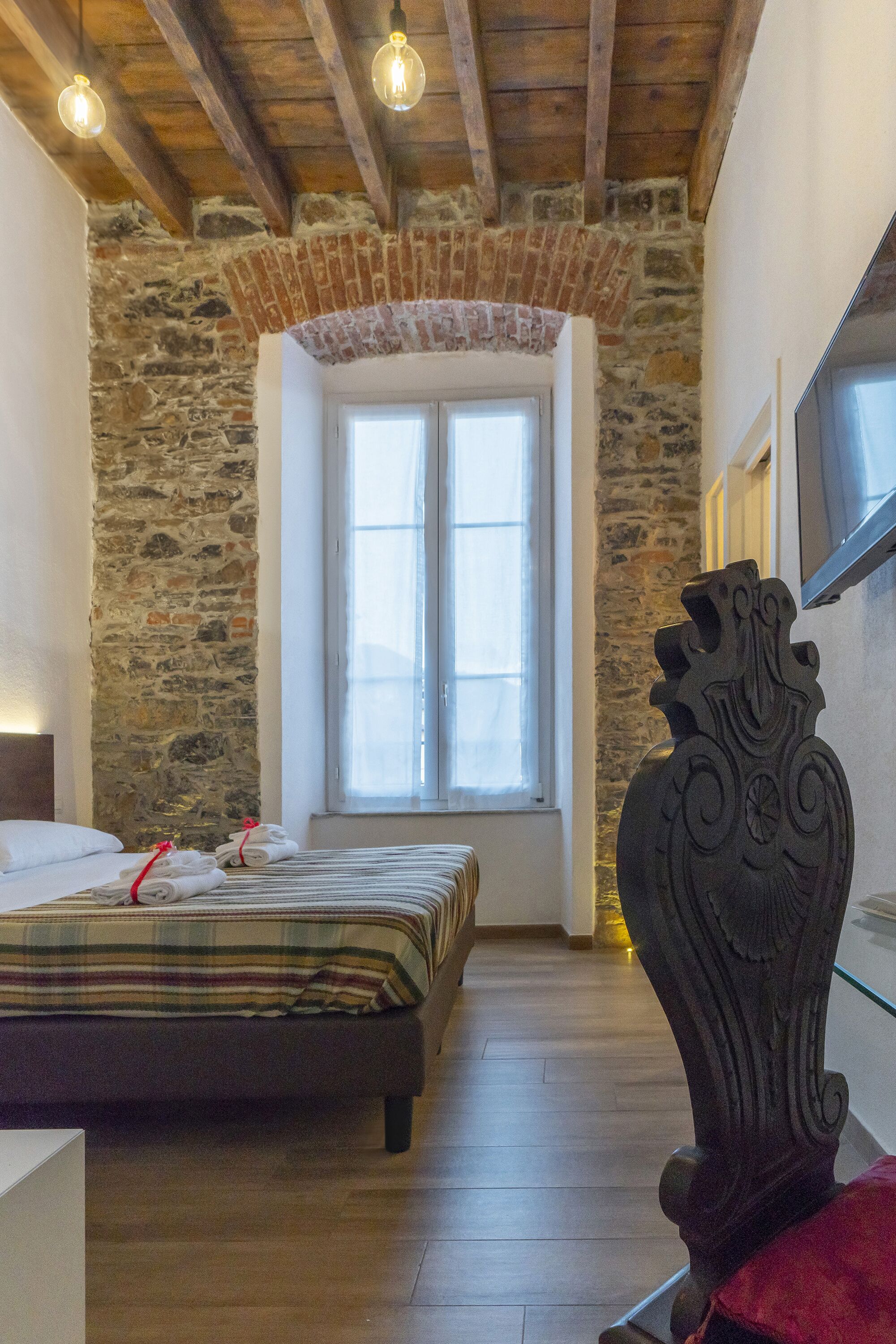 A bedroom with a bed, a stone wall, a window, and a decorative vase.