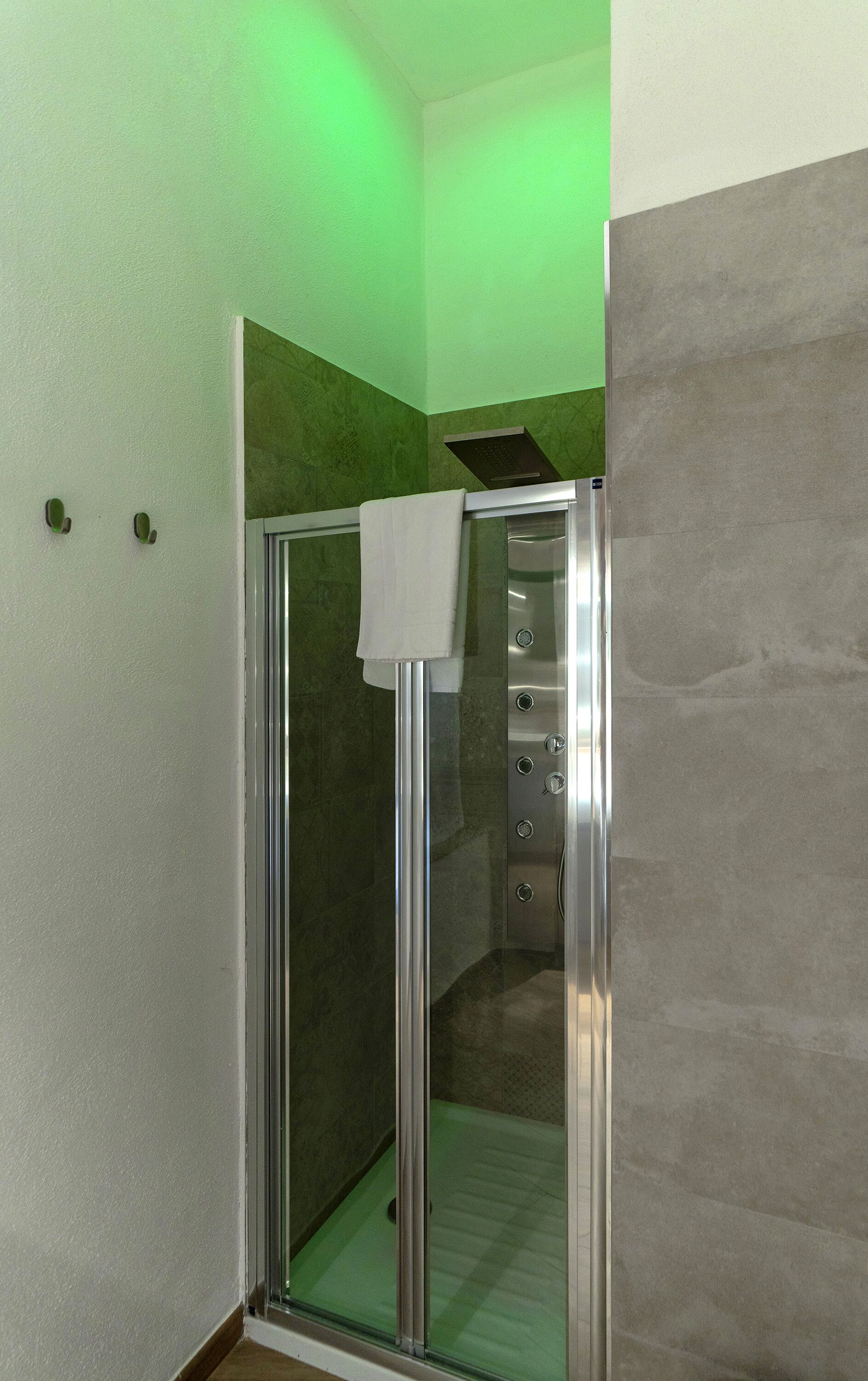 Une cabine de douche moderne avec une porte en verre, une serviette accrochée à la porte et un éclairage vert au-dessus.