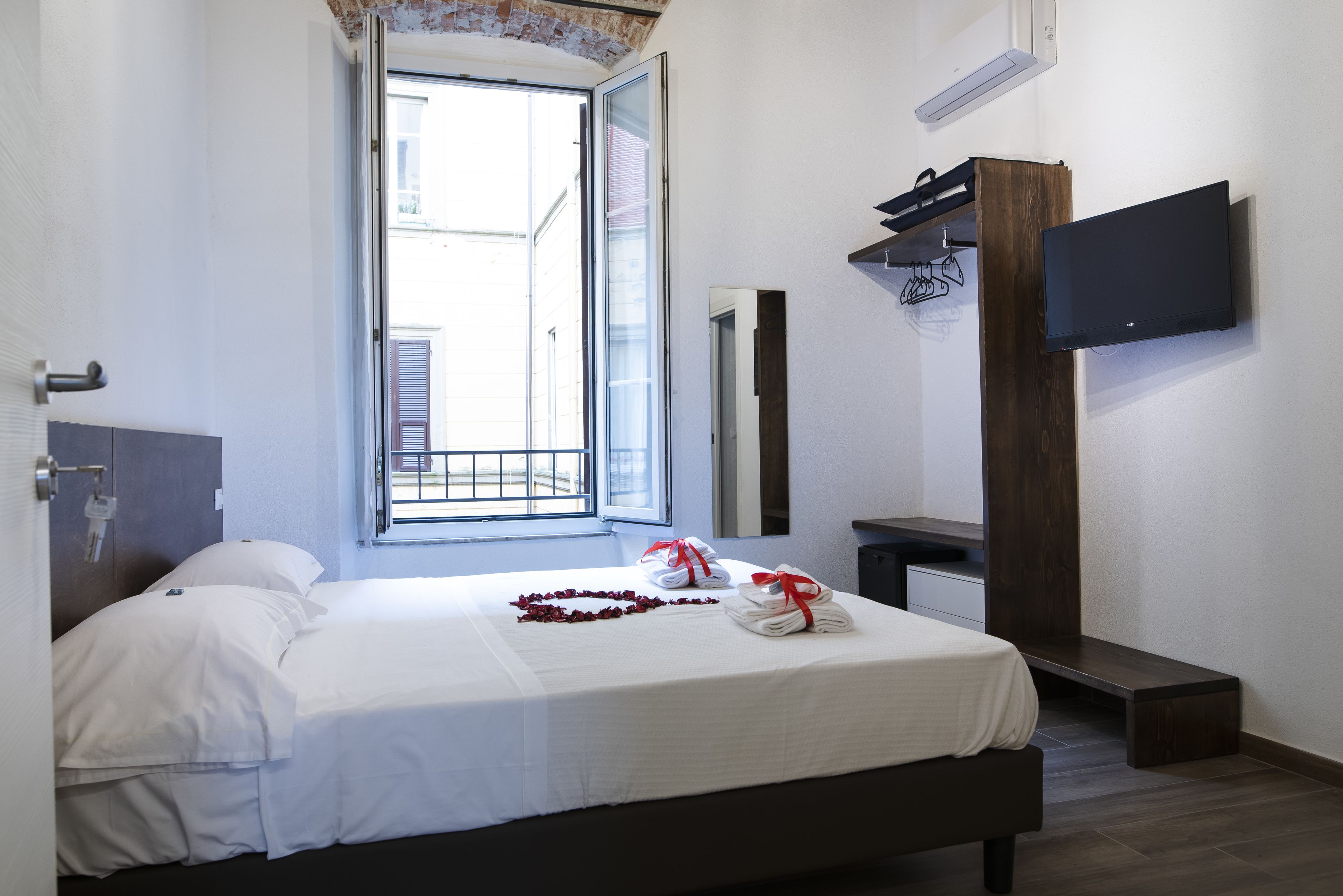 Habitación de hotel con cama, televisor montado en la pared, banca de madera y ventana con vistas al exterior.