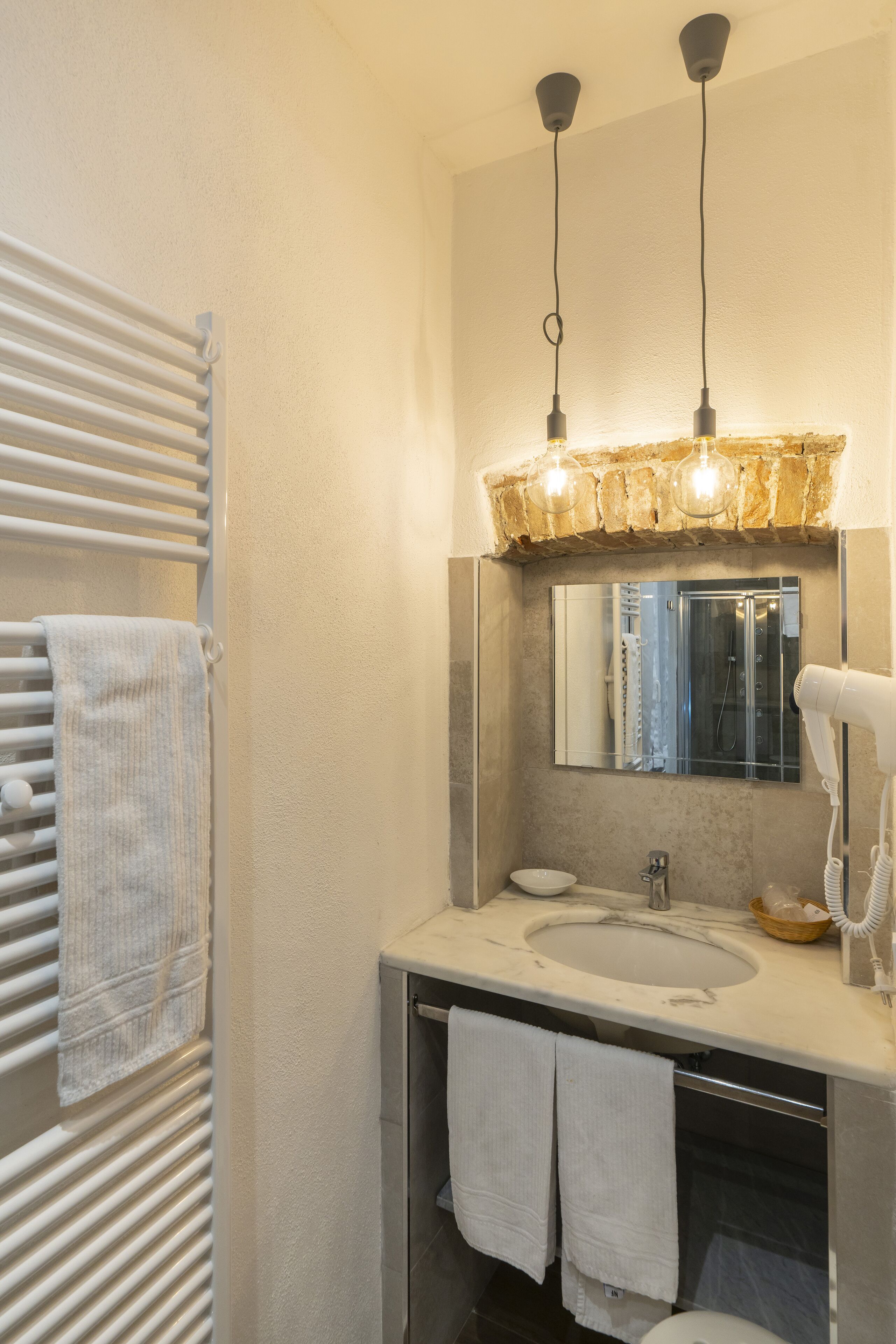 Un baño con lavamanos blanco, espejo, toallero y secador de pelo.