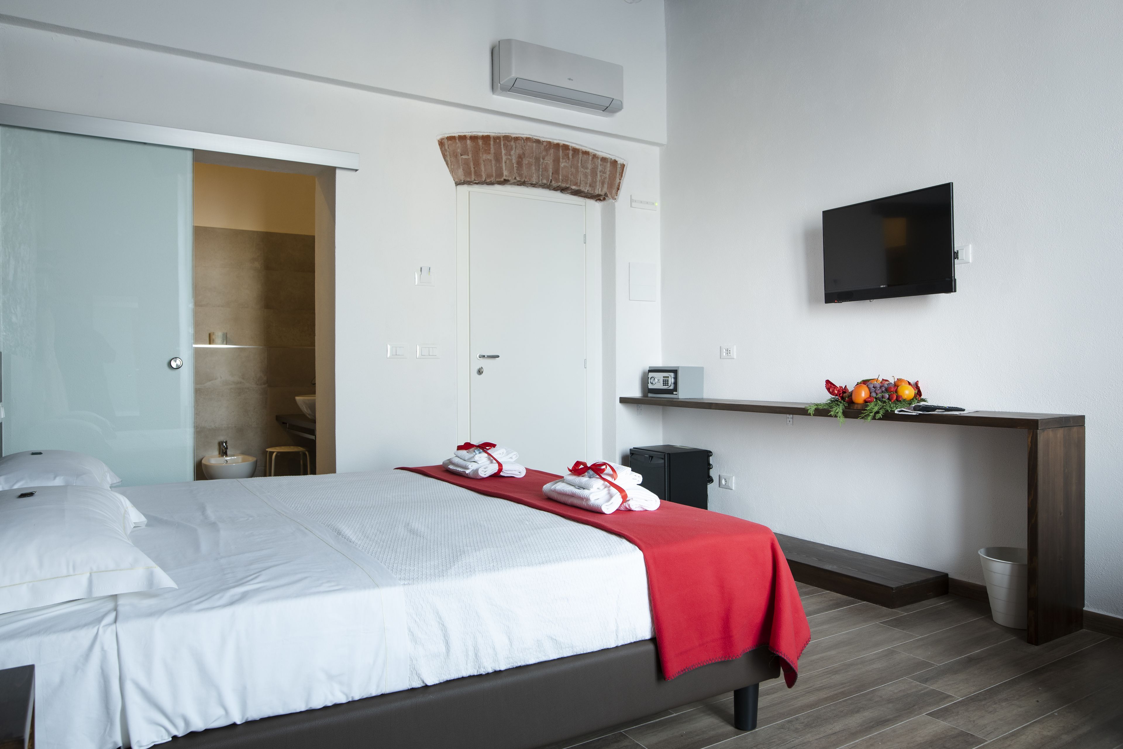 Habitación de hotel con cama, escritorio con televisor, un pequeño cubo de basura y un frutero sobre el escritorio.