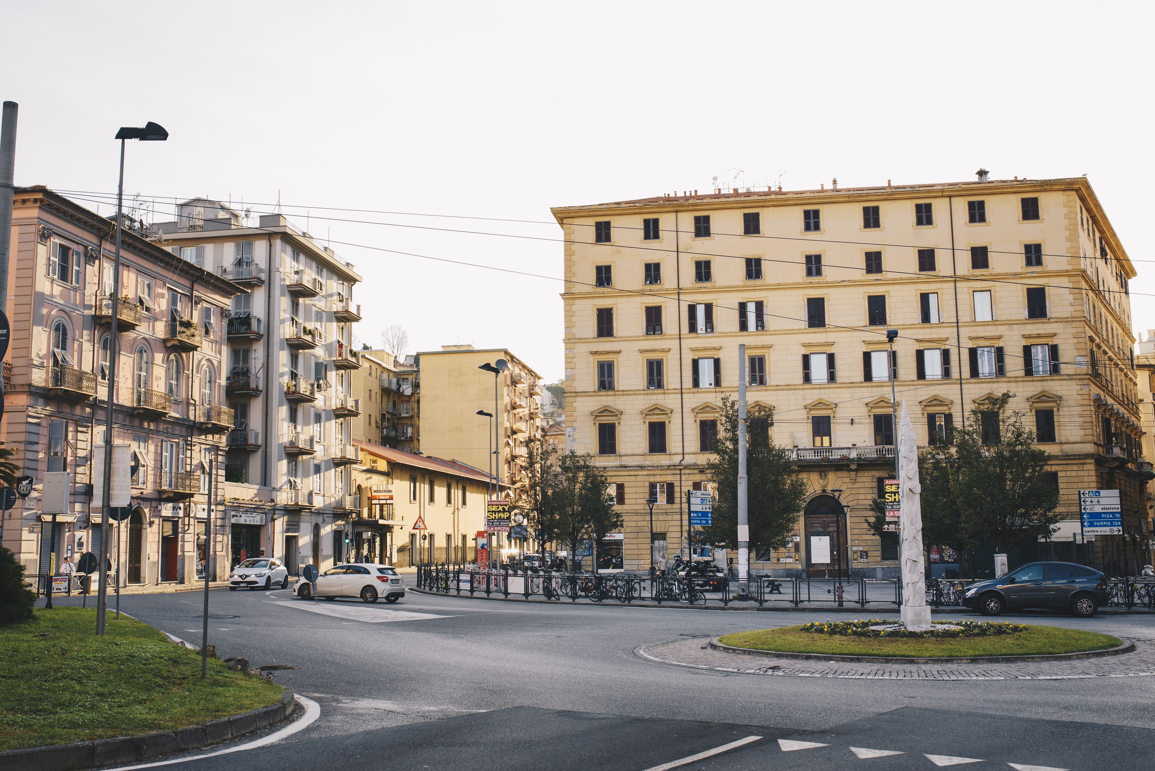 A street view with a roundabout, buildings, and parked cars.