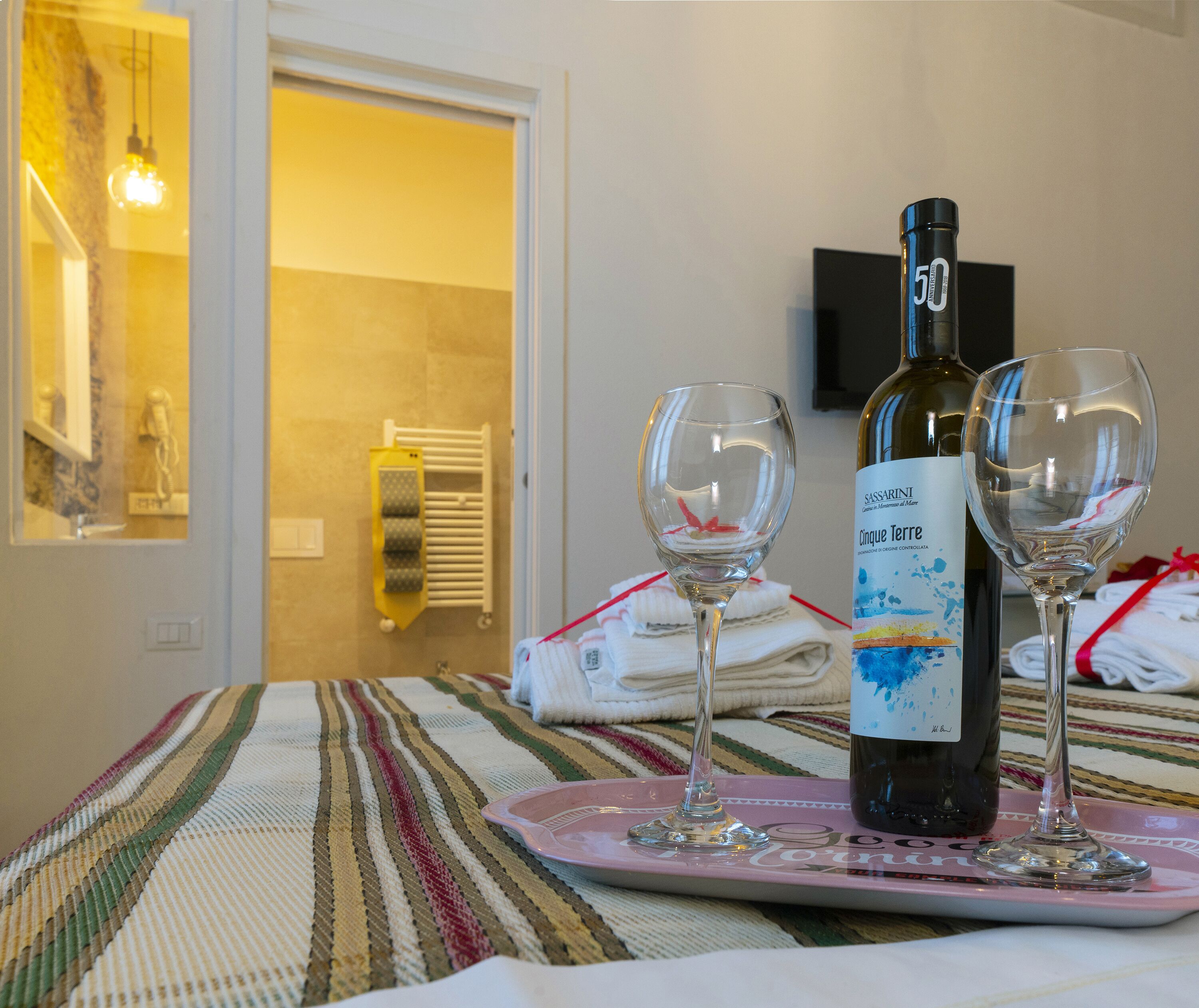 Una botella de vino y dos copas sobre una bandeja rosa en una habitación de hotel.