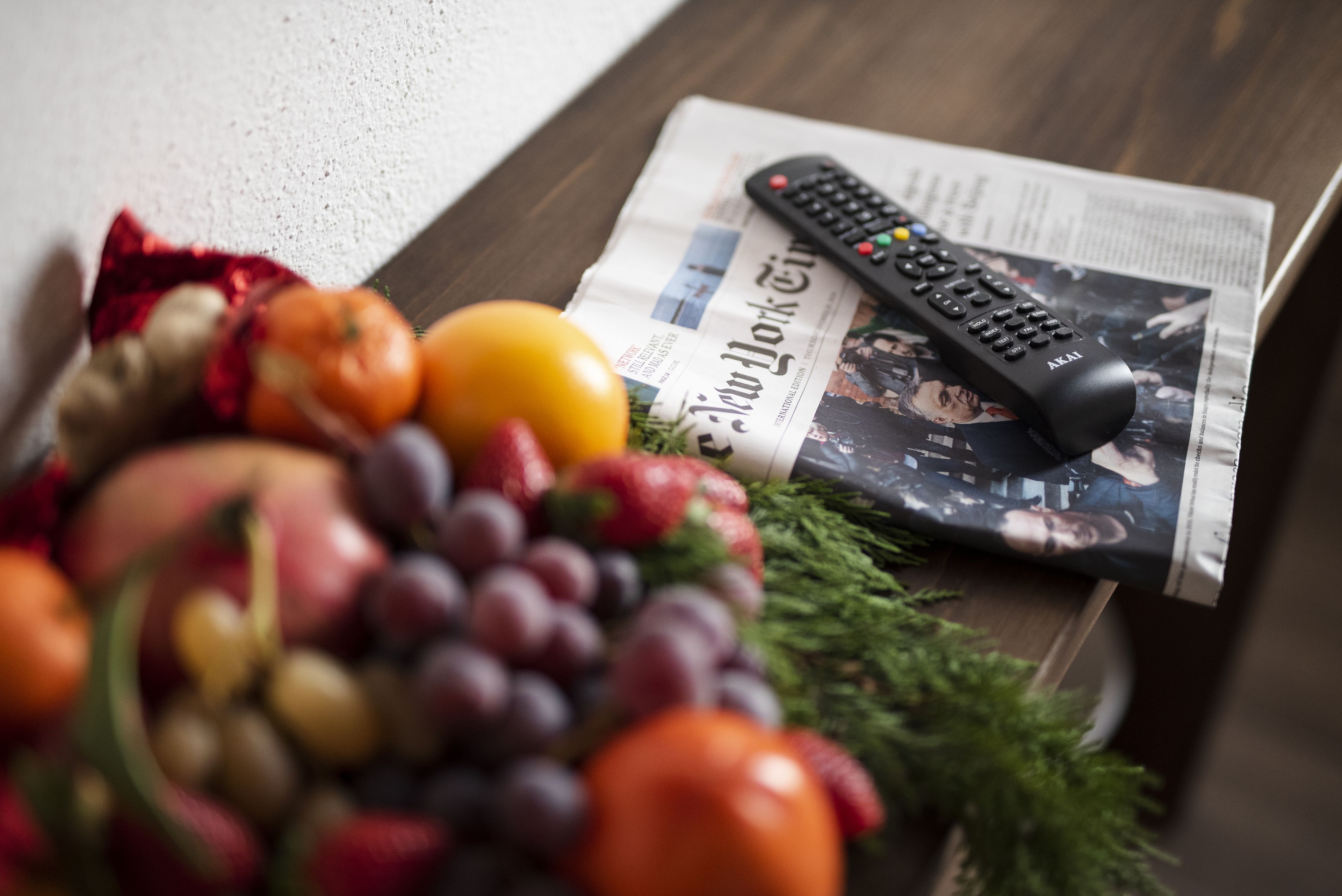 Un control remoto, un periódico y un cuenco con fruta sobre una mesa de madera.